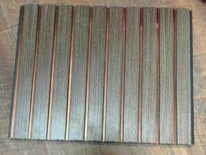Grey wood-texture fluted wall panel with vertical grooves and copper metallic strips.