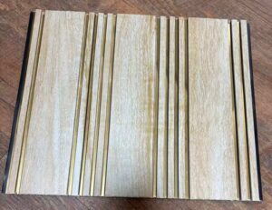 Light beige wood-textured fluted wall panel with vertical golden metallic strips for modern interior decoration.