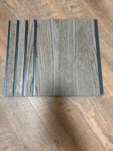 Grey wood-texture fluted wall panel with vertical grooves and dark recessed lines.