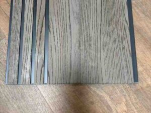 Grey wood-texture fluted wall panel with vertical grooves and dark recessed lines.