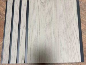 : Light beige wood-texture decorative wall panel with vertical grooves and subtle dark grain detailing.