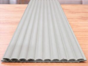 White fluted wall panel with a vertical ribbed design displayed on a wooden table