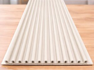 White fluted wall panel with vertical linear grooves displayed on a wooden surface in a modern living room.