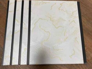 White marble finish fluted wall panel with elegant golden vein patterns and dark grey vertical grooves.