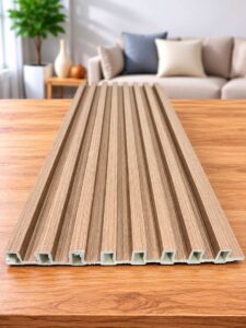 Beige wood-grain slatted wall panel displayed on a wooden table in a modern living room.