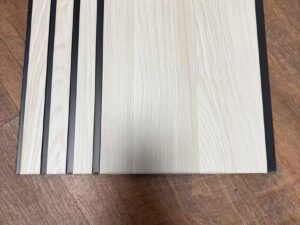 Light white wood-texture fluted wall panel with wide vertical sections and dark recessed grooves.